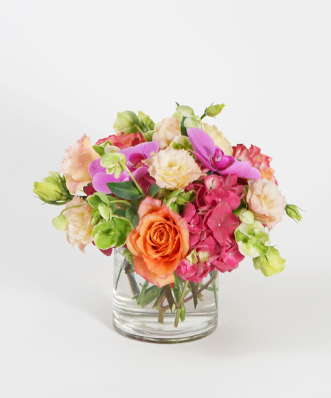 low and lush floral design of hot pink hydrangea, orange roses, and peach lisianthus in a clear glass vase