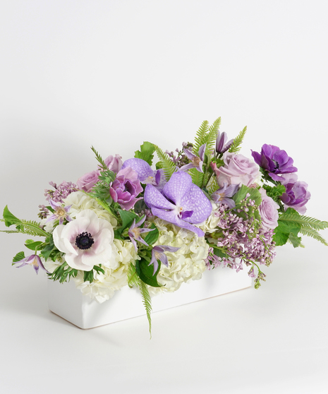 lavender orchids, clematis and lilac centerpiece in white rectangular container