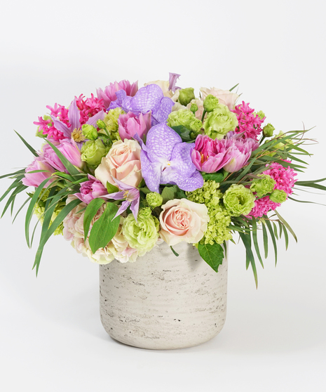 lavender tulips, peach roses, and pink hyacinth arranged in a grey stone container and accented with textural greens