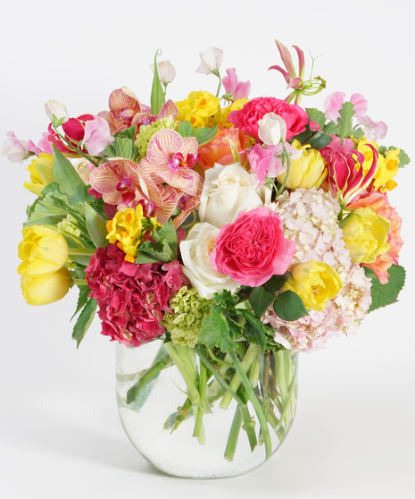 luxury floral design of colorful citrus toned blooms including pink hydrangea, orange roses, mimosa flower and green orchids