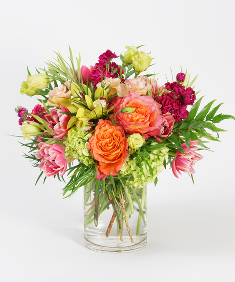 pink hydrangea, orange roses and green orchids arranged in a clear glass vase