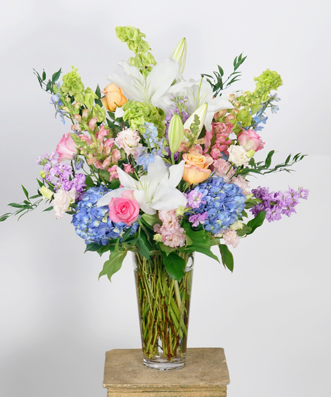 funeral service arrangement of pastel flowers including pink roses, white lilies, and blue hydrangea 