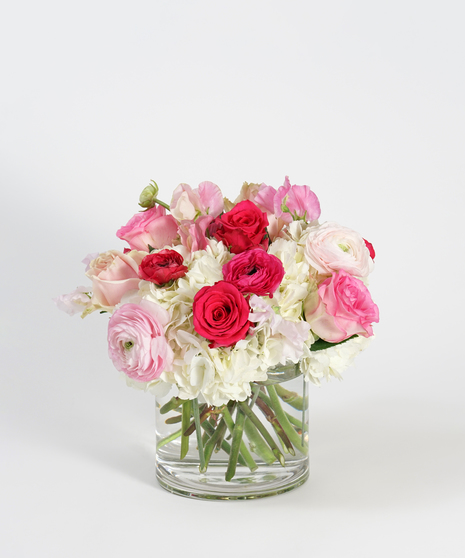 white hydrangea, pink roses and hot pink ranunculus arranged in a clear glass vase