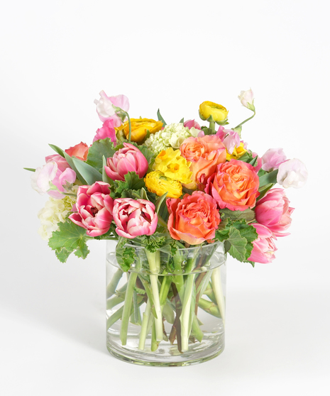 spring floral design of  pink tulips, orange roses, and yellow ranunculus accented with daffodils and seasonal greens